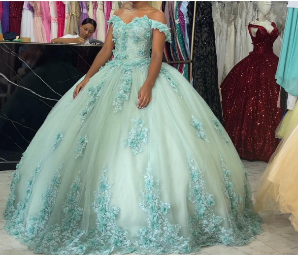 Mujer luciendo un vestido de gala verde claro con bordados florales azules en una tienda de vestidos.