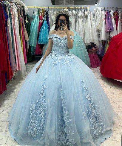 Mujer con vestido de gala azul claro con hombros descubiertos, de pie en una tienda de vestidos.