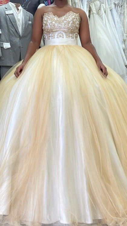 Mujer con un vestido de gala dorado y blanco con corpiño adornado, en una tienda de novias.