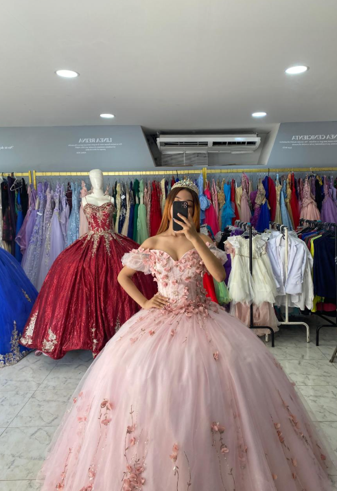 Mujer con vestido de gala rosa con detalles florales, en una tienda de vestidos.