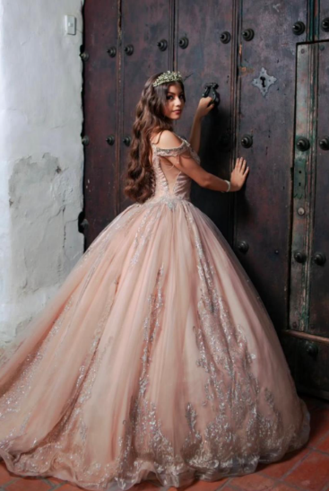 Una mujer con un vestido de gala rosa y una tiara toca una puerta de madera.