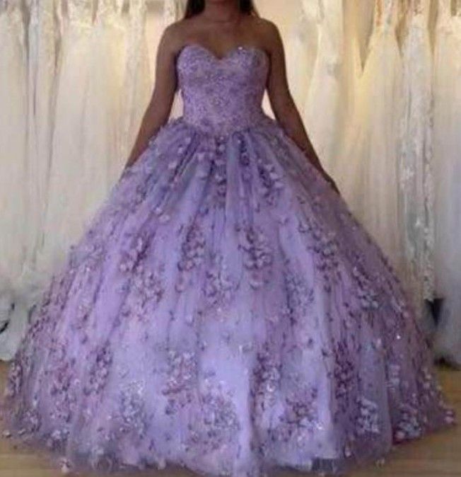 Mujer con un vestido de gala palabra de honor color lavanda con adornos florales; vestidos al fondo.
