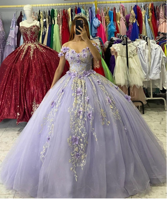 Mujer con vestido de gala color lavanda, selfie frente al espejo, detalles florales. Vestidos al fondo.