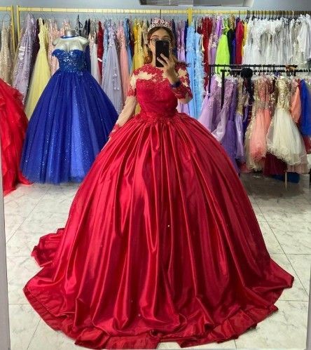 Una mujer con un vestido de gala rojo, sosteniendo un teléfono, está de pie en una tienda de vestidos.