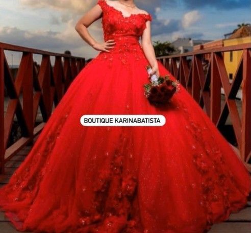 Mujer con vestido de gala rojo, sosteniendo flores, en un puente, posando para la cámara.