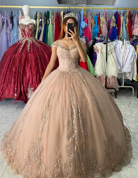 Mujer con un vestido de gala rosa pálido, tomándose una selfie. Al fondo, una boutique con percheros repletos de vestidos