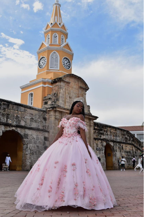 Mujer con vestido de gala rosa posa frente a una torre del reloj en Cartagena, Colombia.