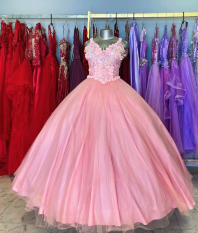 Vestido de gala rosa con corpiño floral expuesto en una tienda de vestidos; al fondo, otros vestidos coloridos.
