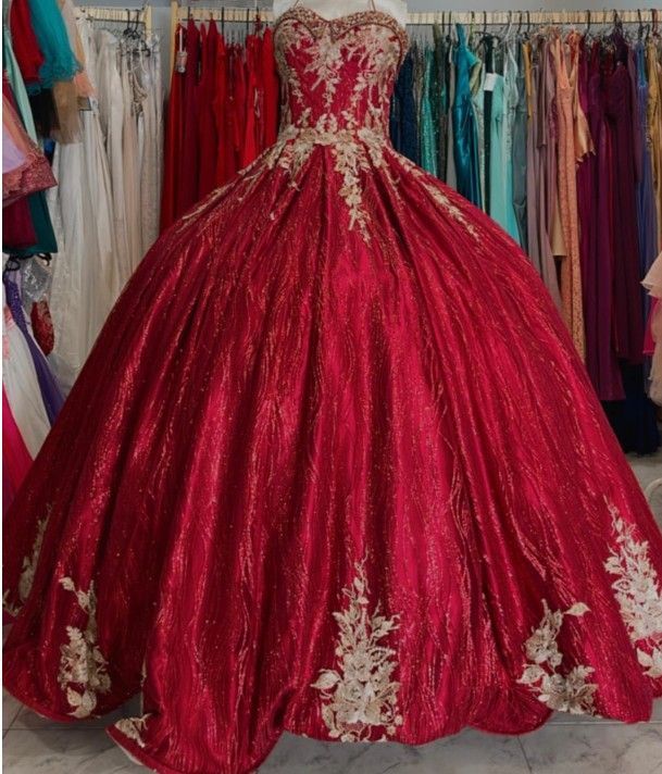 Vestido de gala rojo y dorado con corpiño bordado y falda amplia, colgado en una tienda de vestidos.