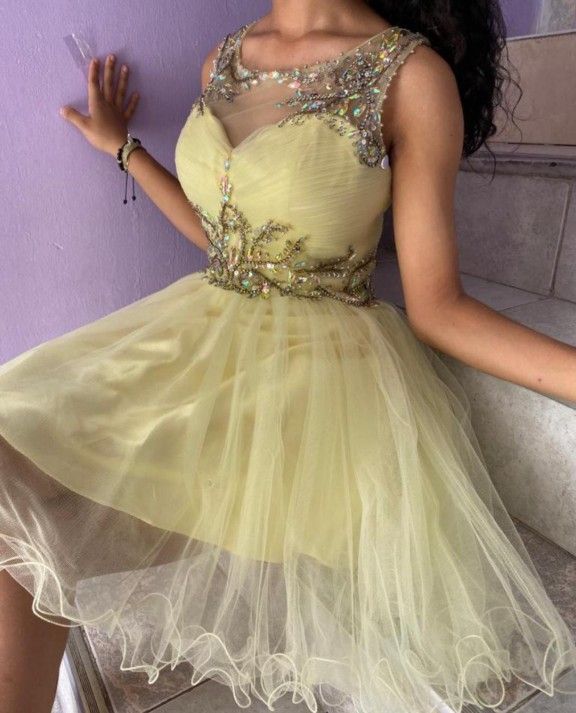 Mujer con un vestido corto de tul amarillo con corpiño de cuentas, posando en unas escaleras cerca de una pared morada.