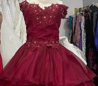 Vestido de gala color burdeos con escote barco, corpiño adornado y falda de tul en capas, expuesto en una tienda.