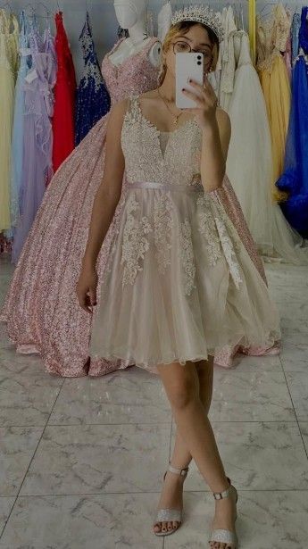 Mujer con vestido corto de gala adornado, sosteniendo un teléfono, con vestidos al fondo.