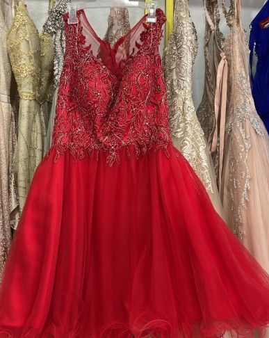 Vestido rojo de gala con corpiño de cuentas y falda de tul, colgado en una tienda junto a otros vestidos.