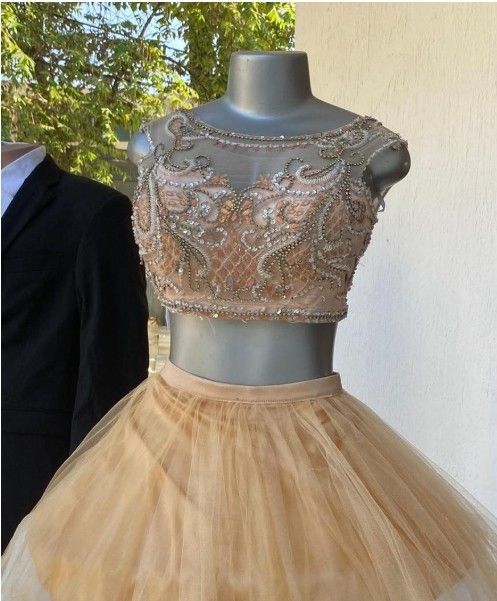 Vestido formal de dos piezas sobre un maniquí; top corto color canela con cuentas y falda de tul en capas.
