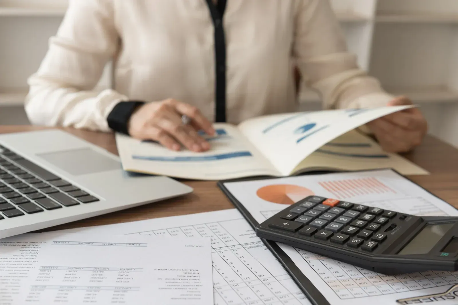 A woman is sitting at a desk with a laptop and a calculator.