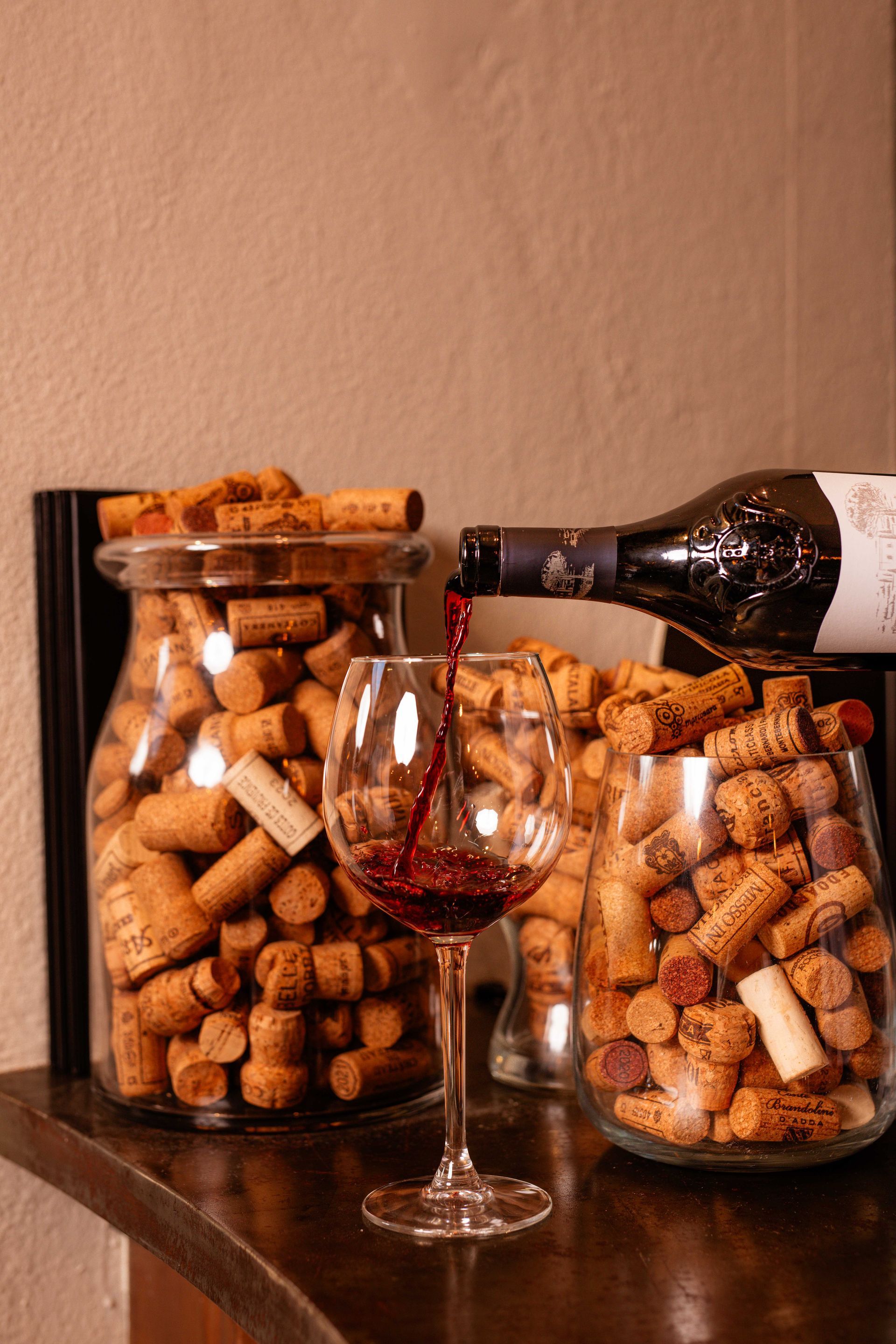 Una bottiglia di vino viene versata in un bicchiere accanto a un barattolo di tappi di sughero.