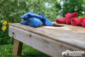 A wooden cornhole board with blue and red bags on it