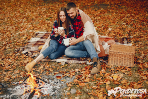 A man and a woman are sitting on a blanket next to a fire.