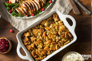 A casserole dish filled with stuffing next to a plate of chicken.