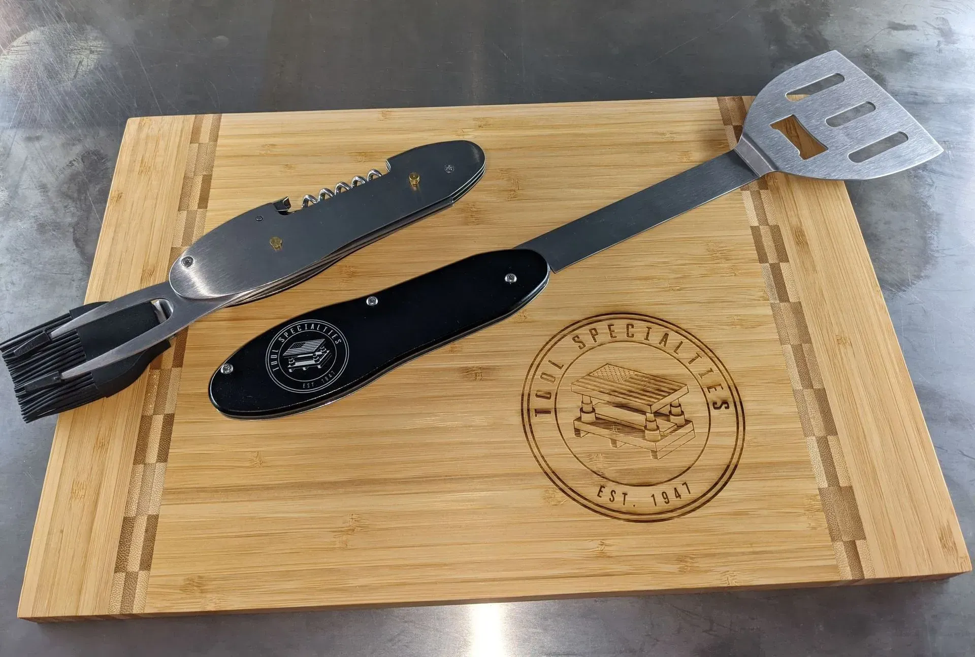 A wooden cutting board with a spatula and tongs on it.