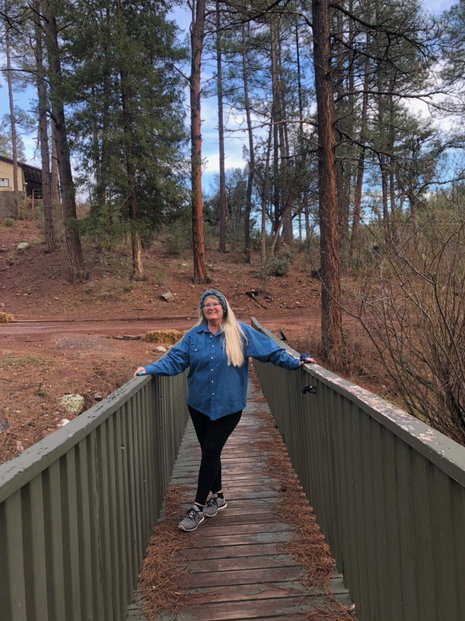 A woman is standing on a wooden bridge in the woods.