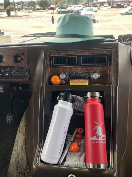 A hat is sitting on the dashboard of a car next to two water bottles.