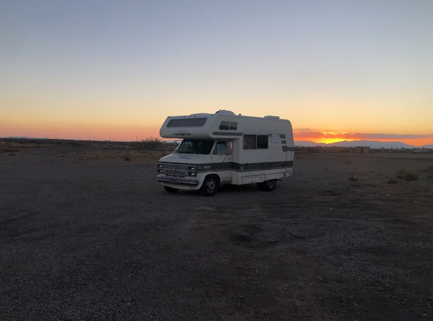 A white rv is parked in the desert at sunset
