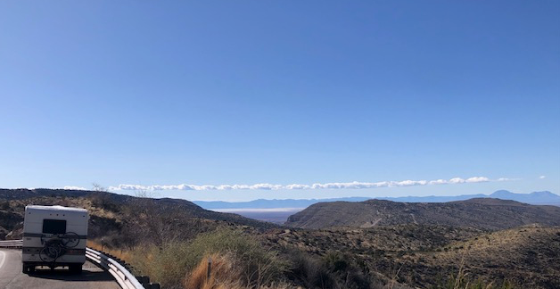 A truck is driving down a road with mountains in the background.