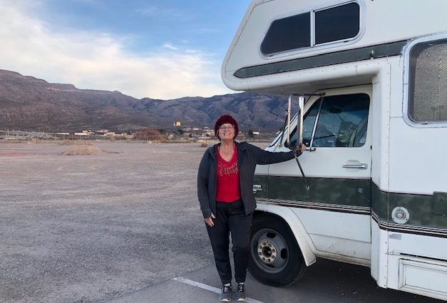 A woman is standing next to a rv in a parking lot.