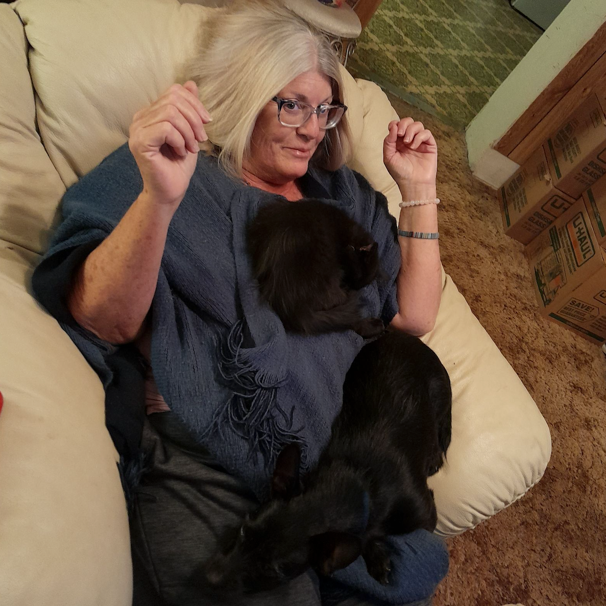 A woman is laying on a couch holding two black dogs