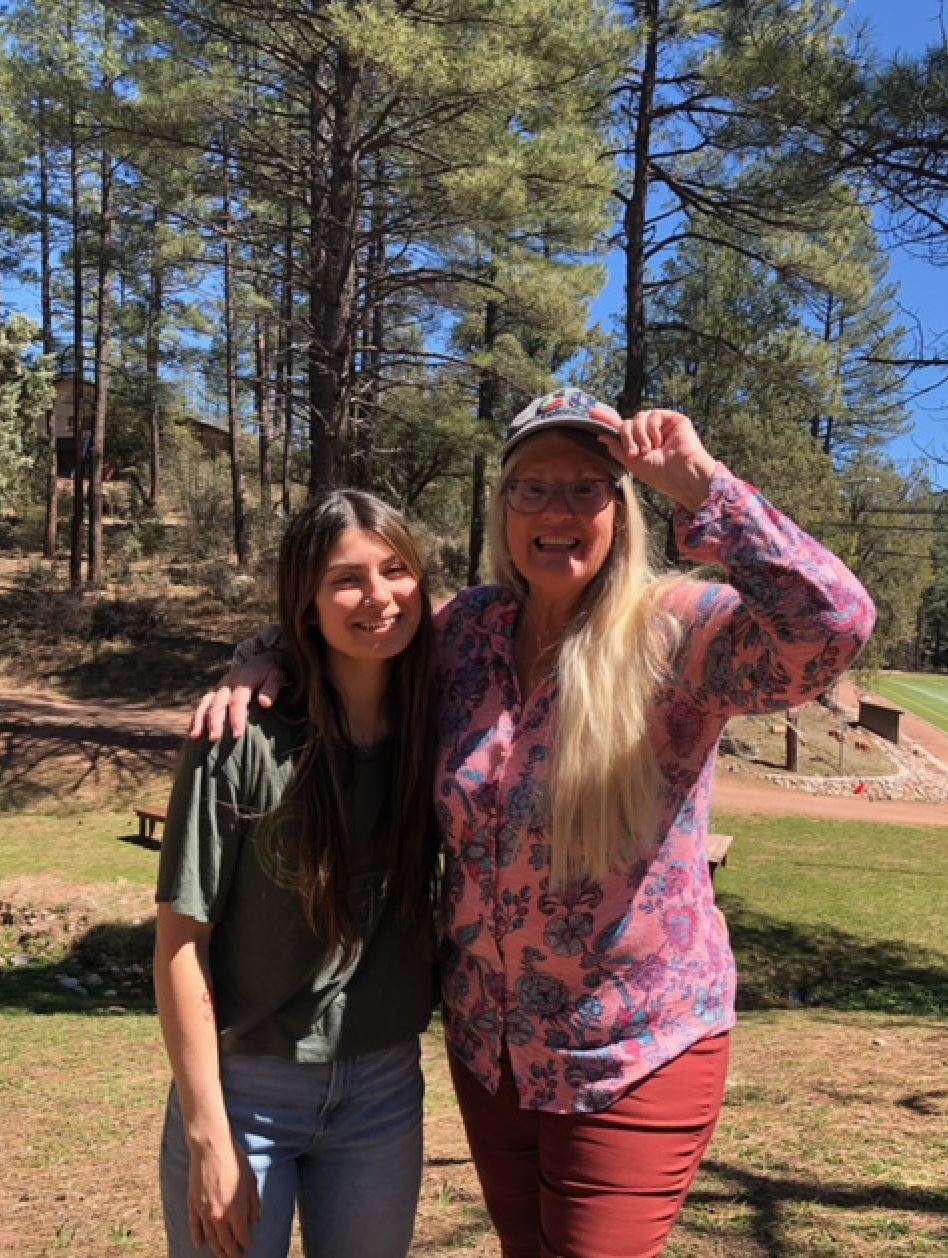 Two women are posing for a picture in front of a forest.