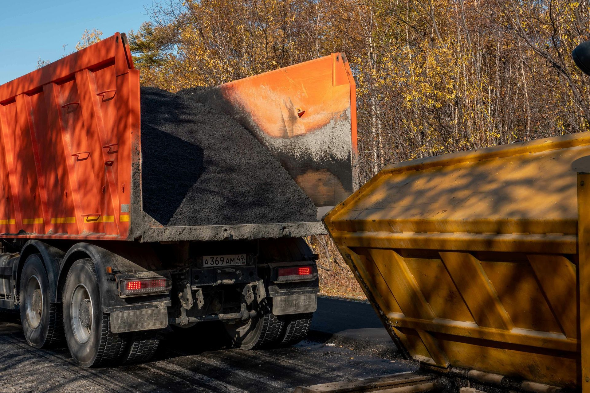 A dump truck filled with coal is parked next to a yellow dumpster.