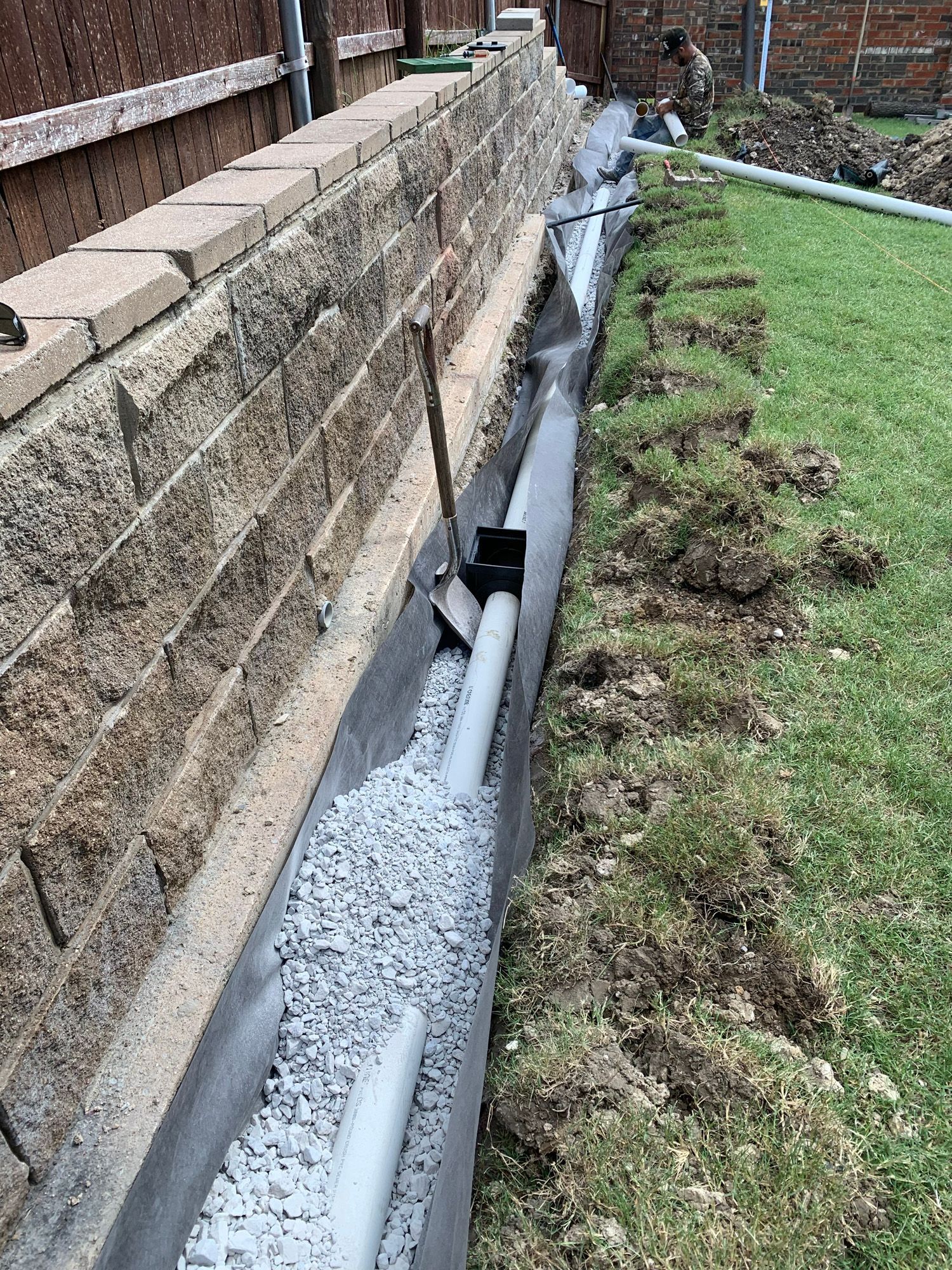 A drainage system is being installed on the side of a brick wall.