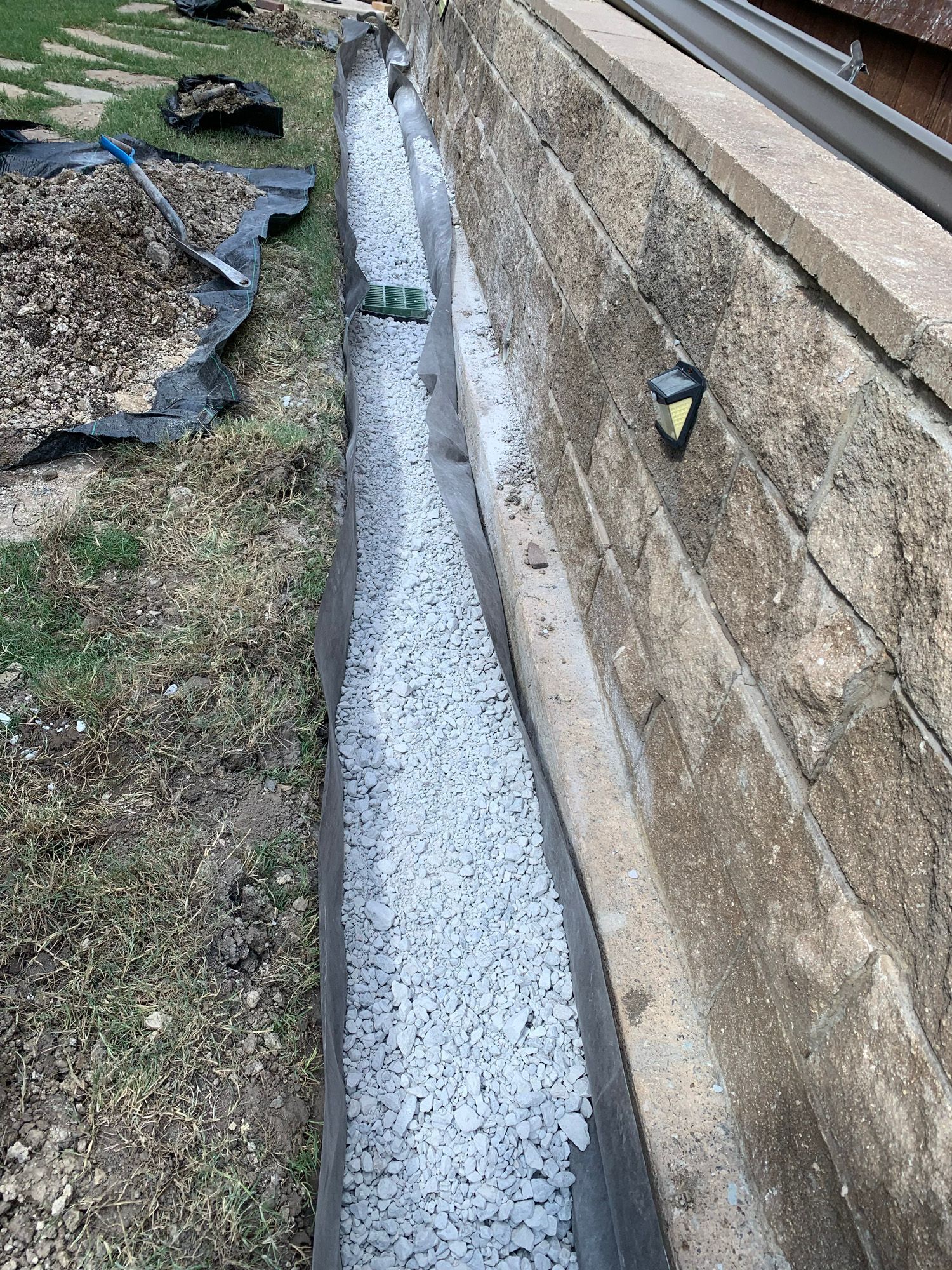 A drainage system is being installed on the side of a brick wall.