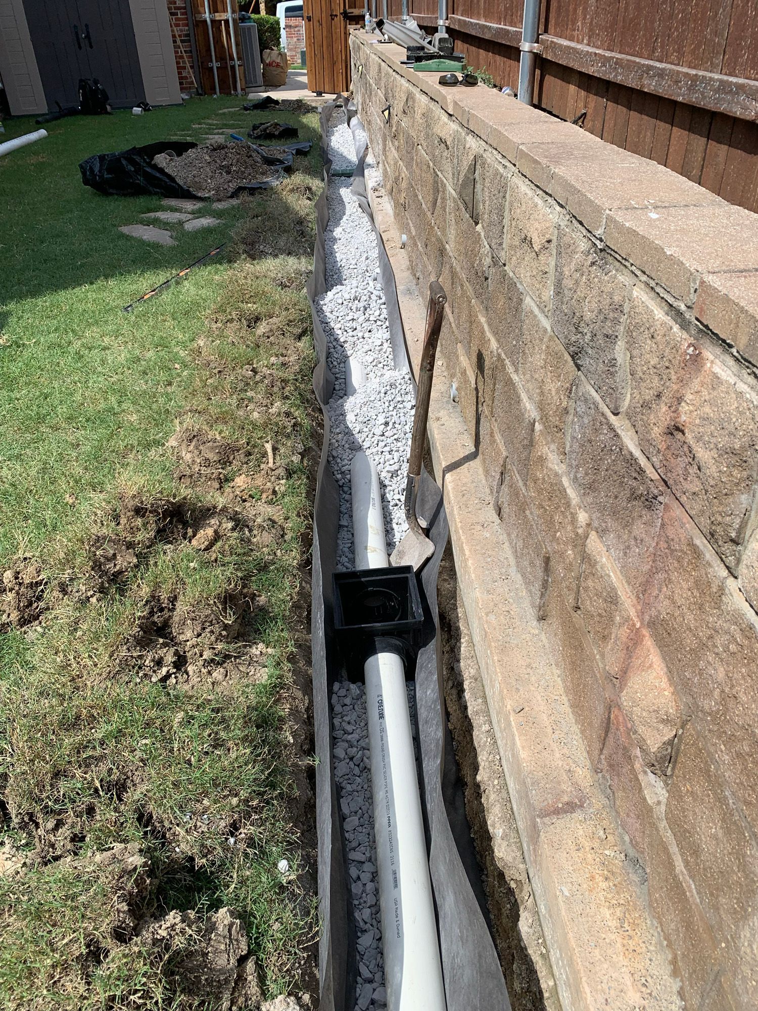 A drainage system is being installed on the side of a brick wall.