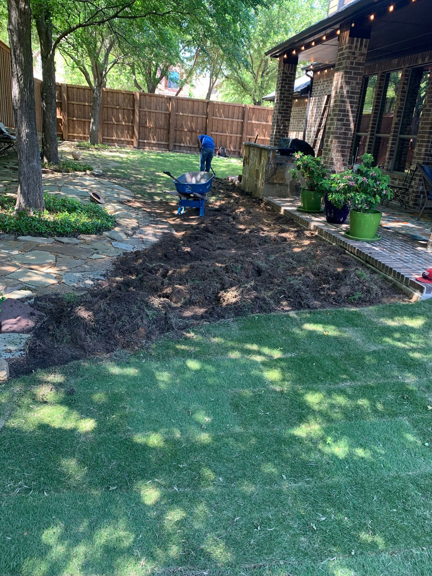 A backyard with a wheelbarrow filled with dirt and a fence in the background.