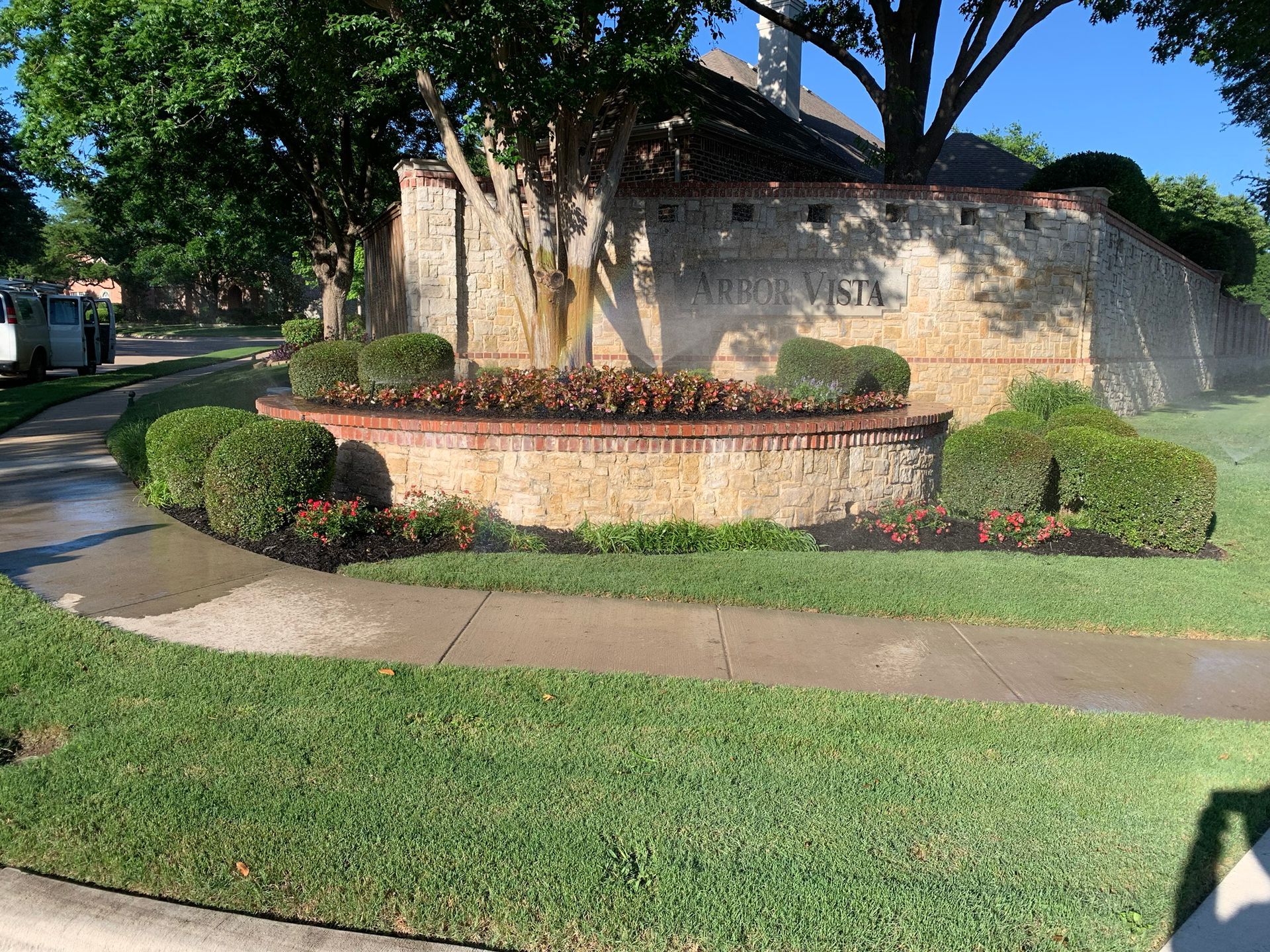A stone wall with flowers and bushes in front of a house.