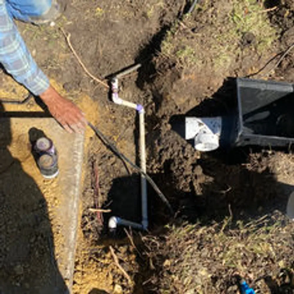 A man is working on a pipe in the dirt.
