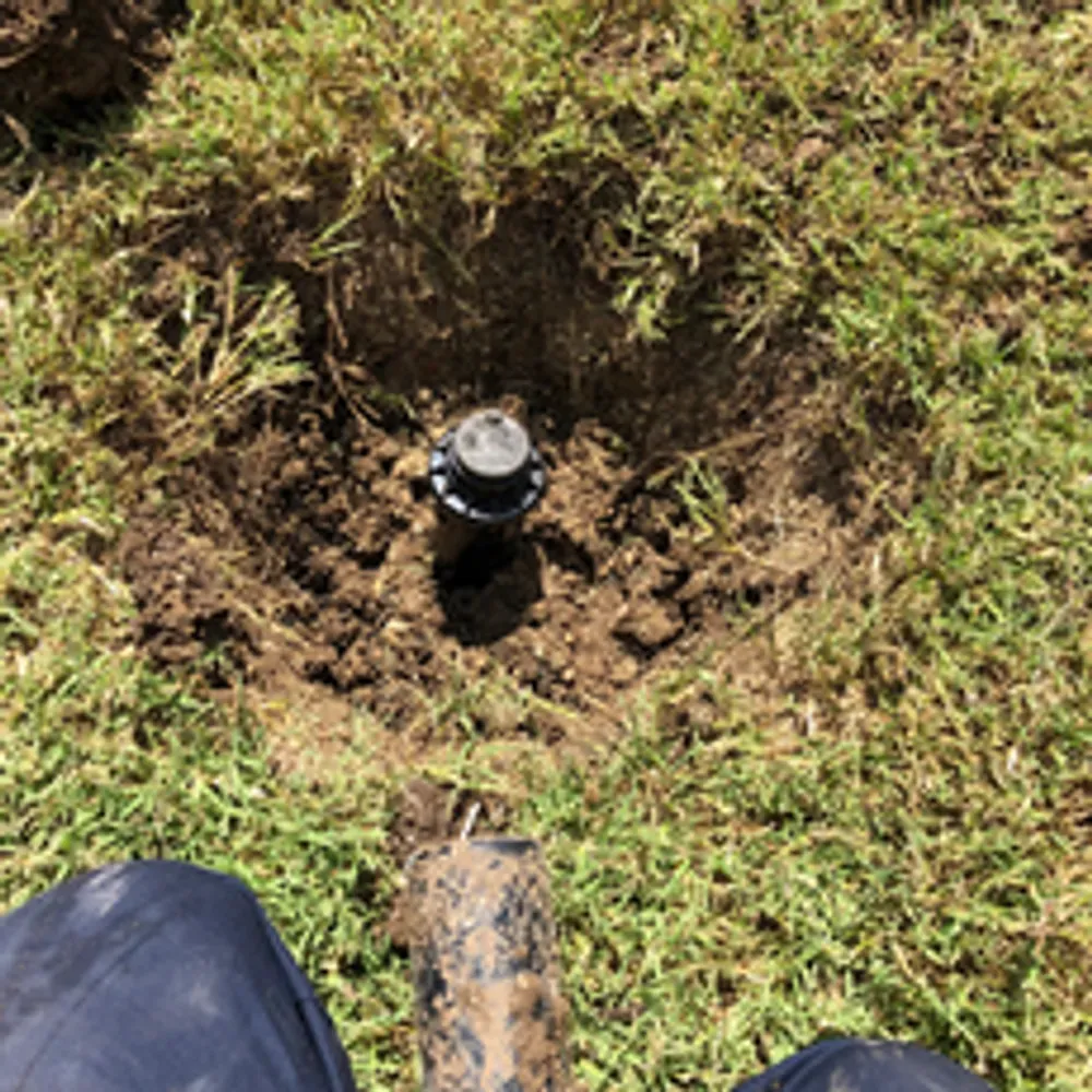 A person is digging a hole in the grass to install a sprinkler.