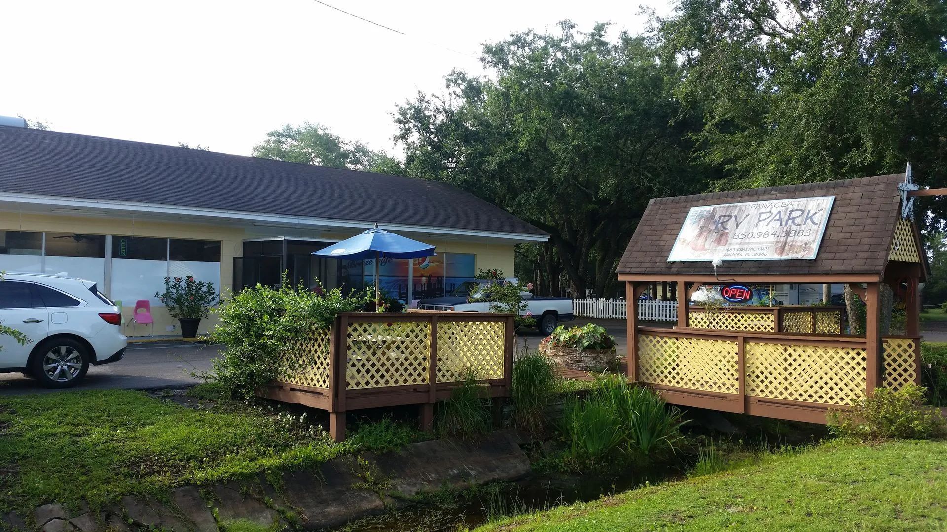 Wooden outdoor deck seating area beside a house, with a blue umbrella and greenery around it