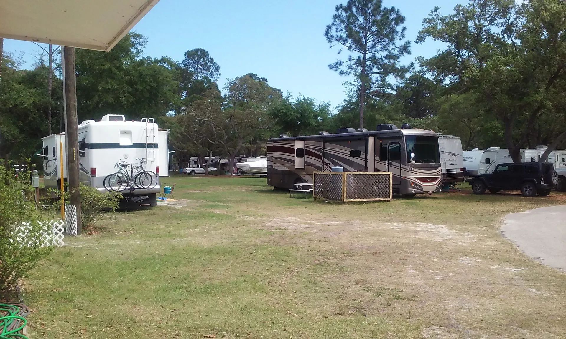 RVs and trailers parked on a grassy lot with trees and a dirt road under a clear sky