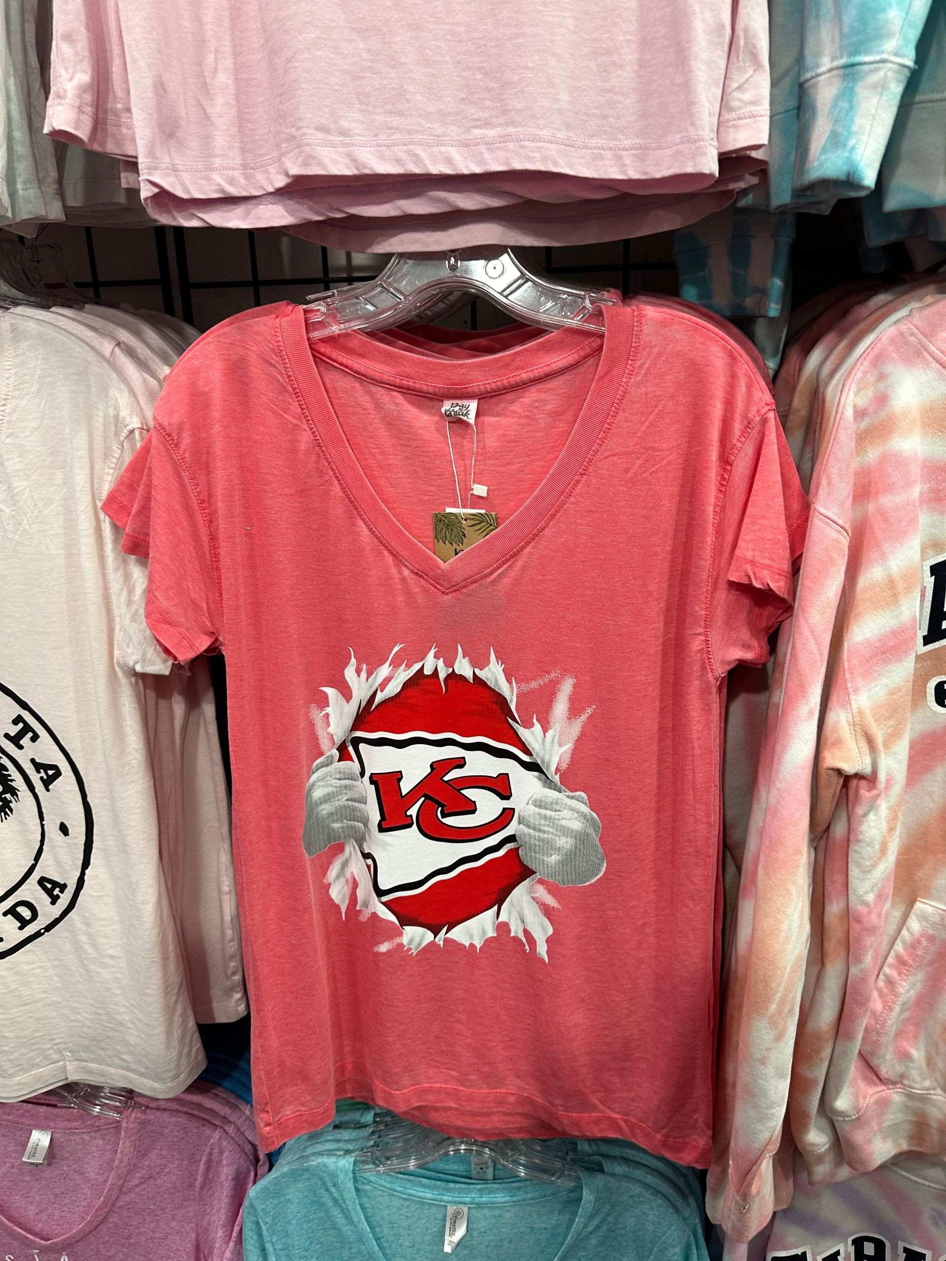 Red Kansas City Chiefs t-shirt with logo, torn effect, and hands. On a clothing rack.