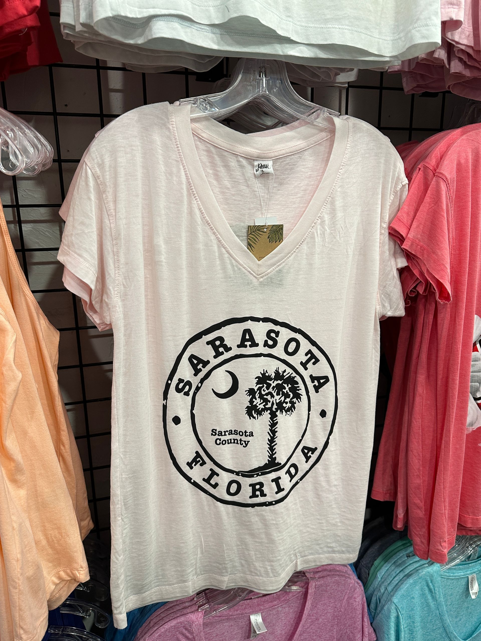 Pink Sarasota, Florida t-shirt with a tree and crescent moon logo, hanging on a rack.