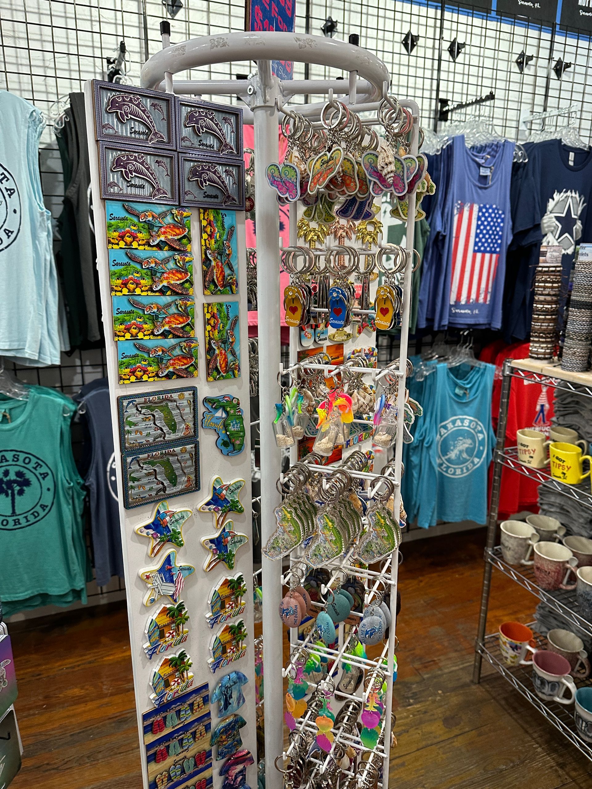 A store display filled with magnets and keychains, with t-shirts and mugs visible in background.