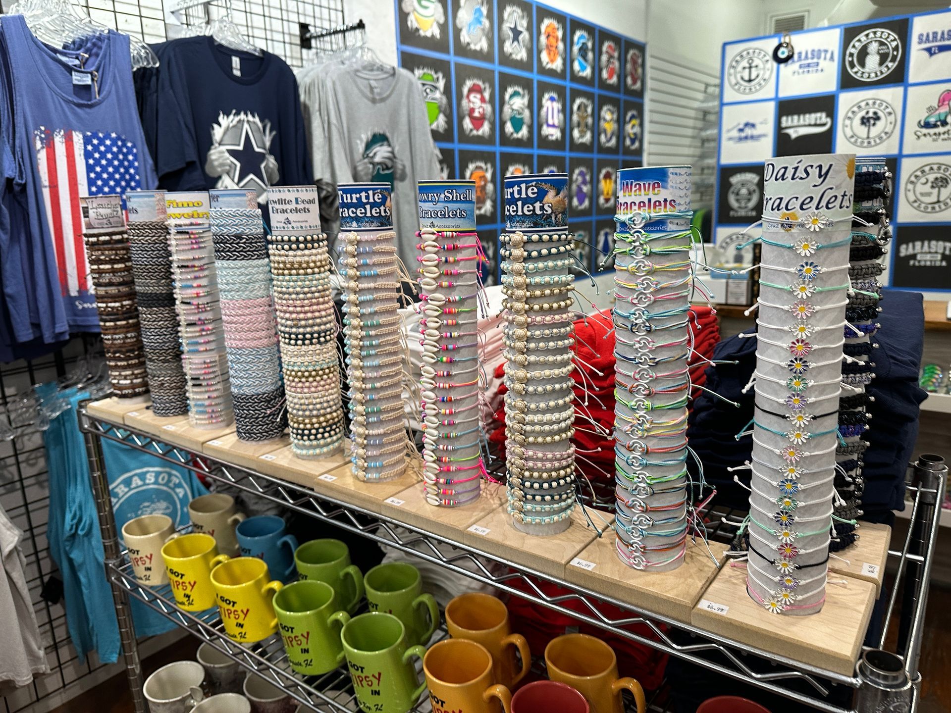 Display of bracelets on a shelf, mugs below, and t-shirts on hangers in a shop.