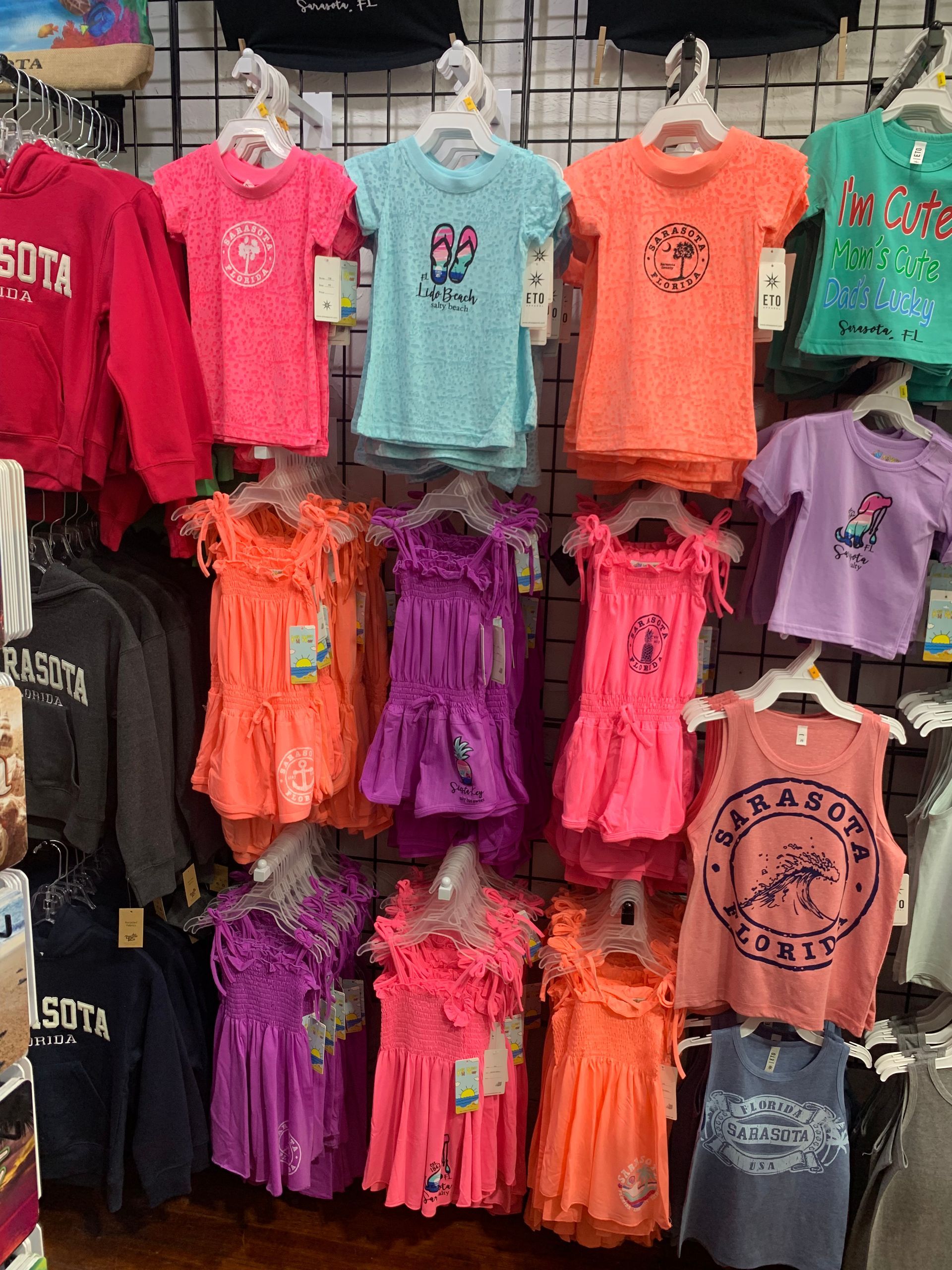 Row of colorful children's clothes, including dresses and shirts, hanging on display in a store.