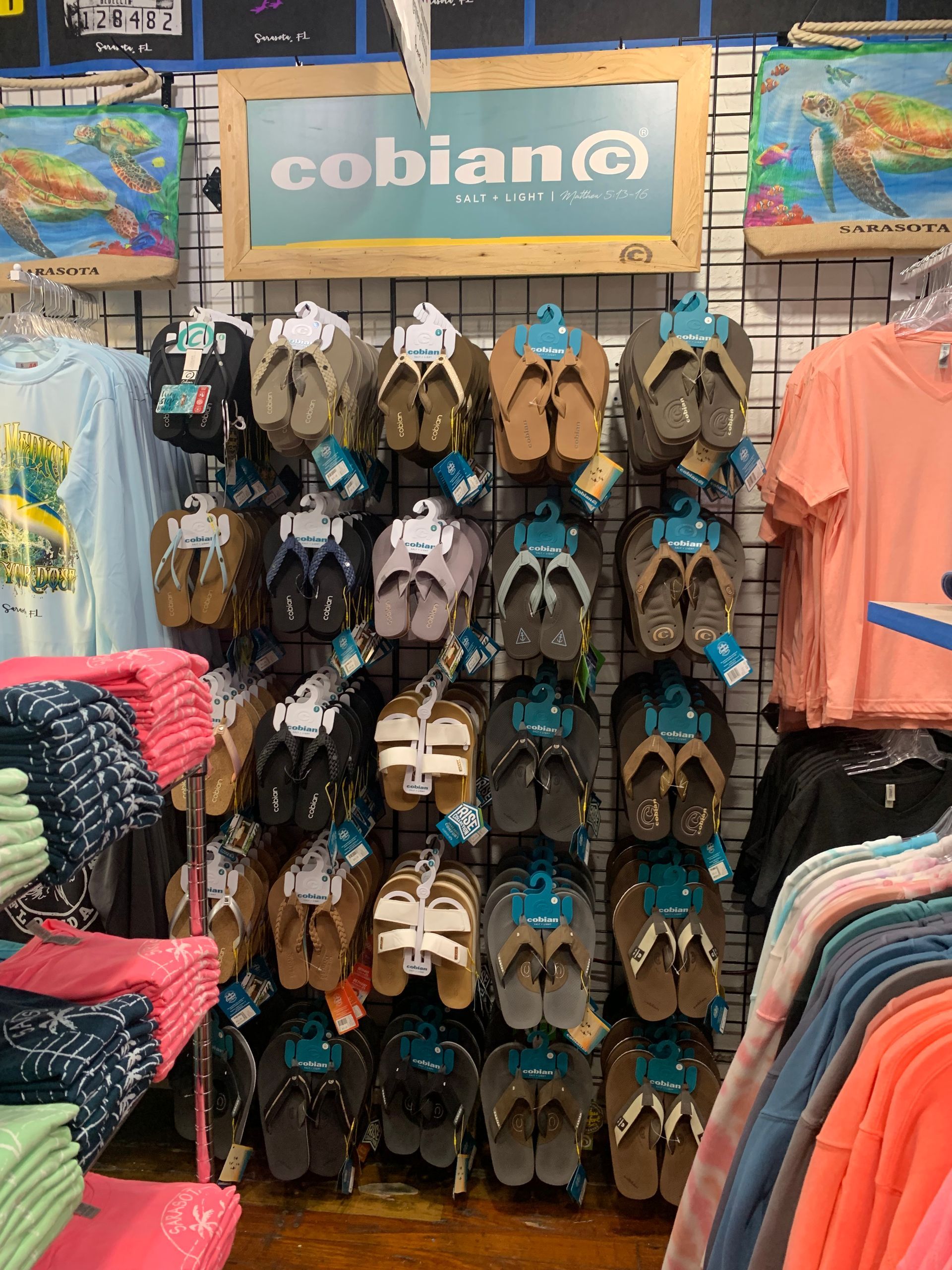 Cobian flip-flops display in a store. Rows of various colors and styles hanging on a wooden background.