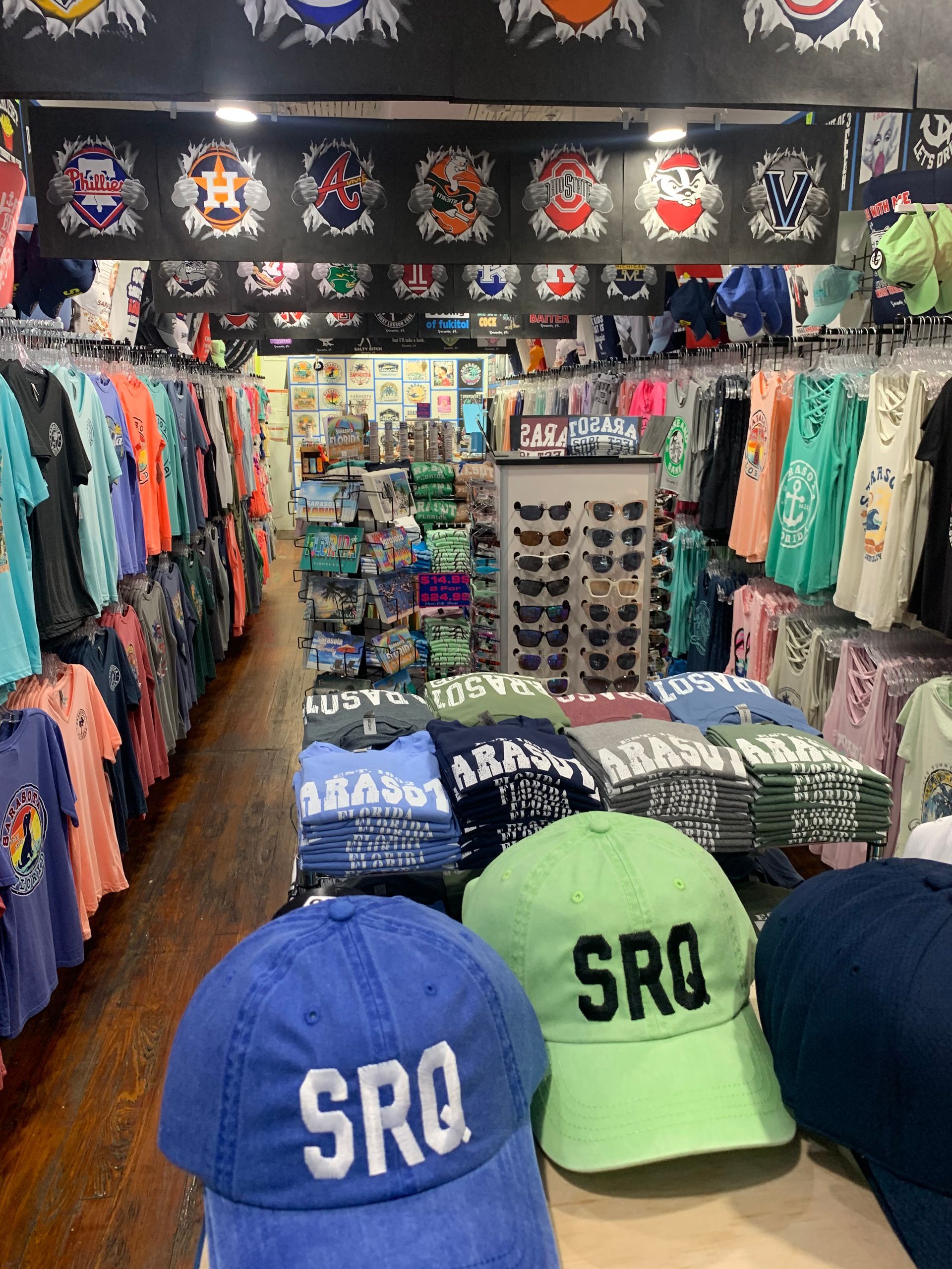 Interior of a souvenir shop with clothing, hats, and sunglasses on display.