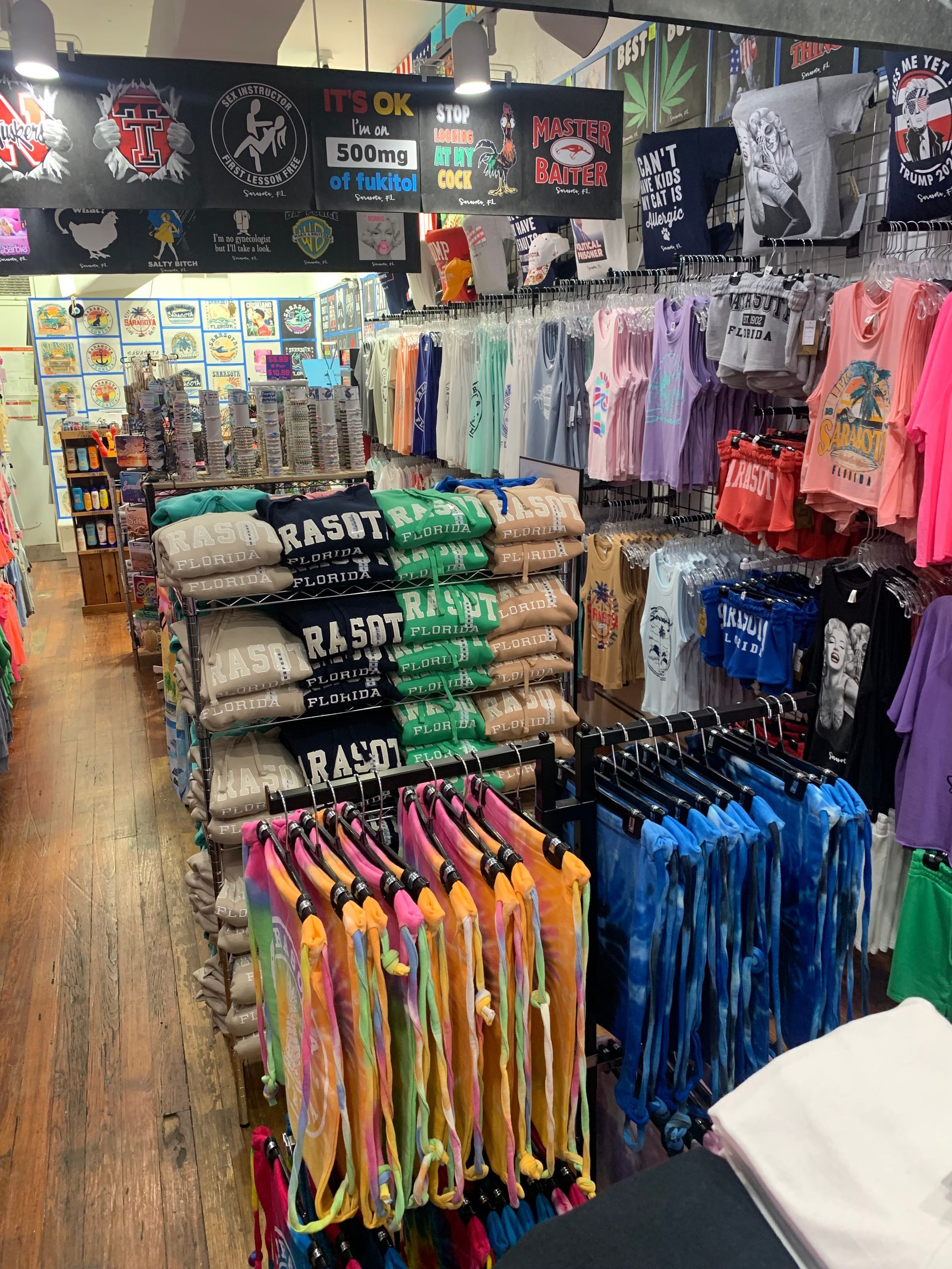 Inside a clothing store, racks display various colorful shirts and pants.