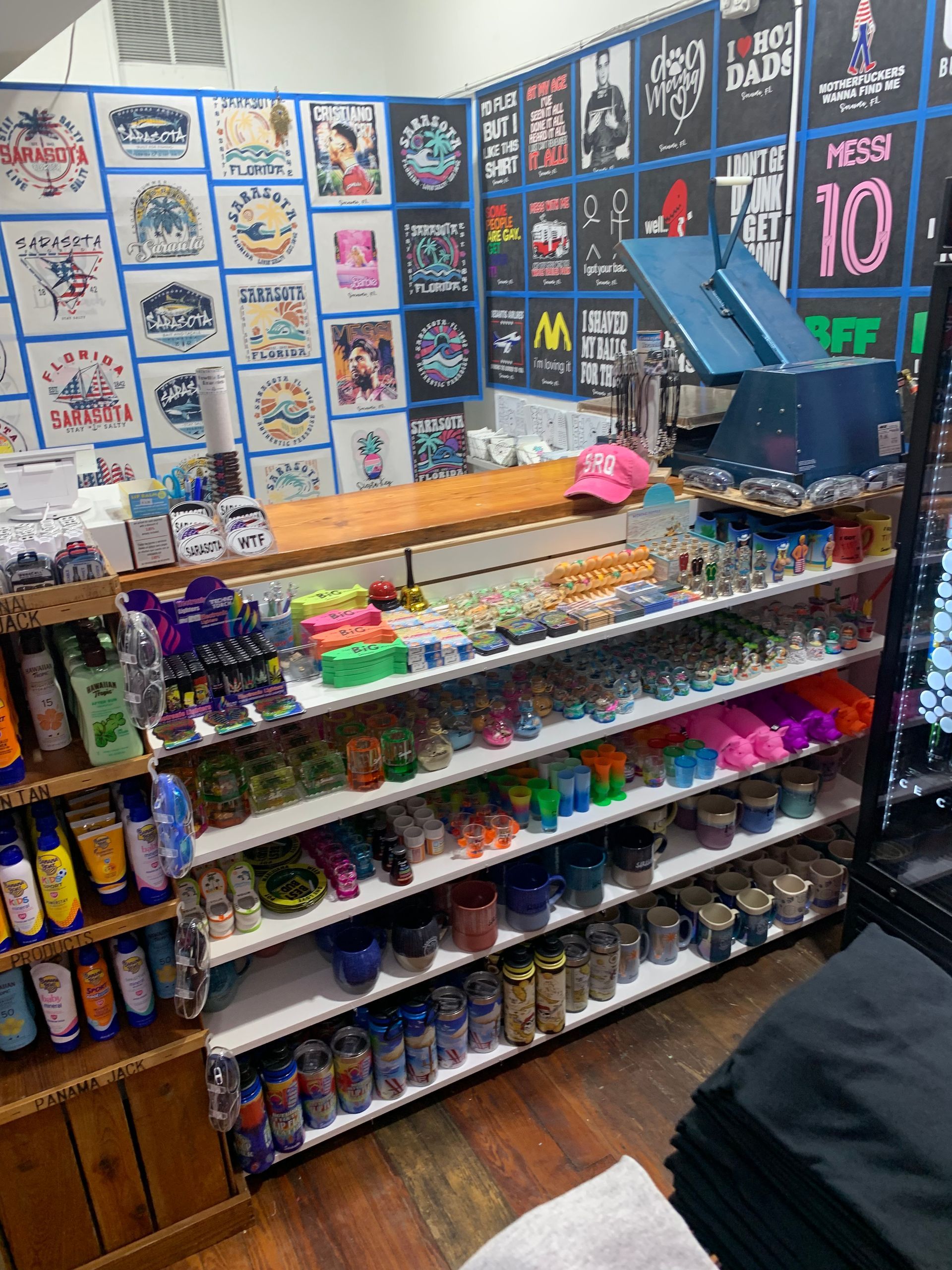 A shop display with shelves of various items, including sunscreen and colorful trinkets, plus t-shirt designs on the wall.